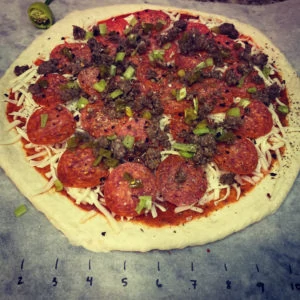 Topped pizza with pepperoni and sausage ready for the grill