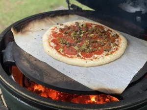 Pizza on parchment sliding onto the pizza stone in the Big Green Egg