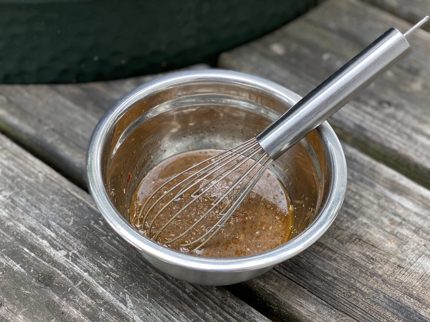 marinade with a whisk in a metal mixing bowl on a rough wood table