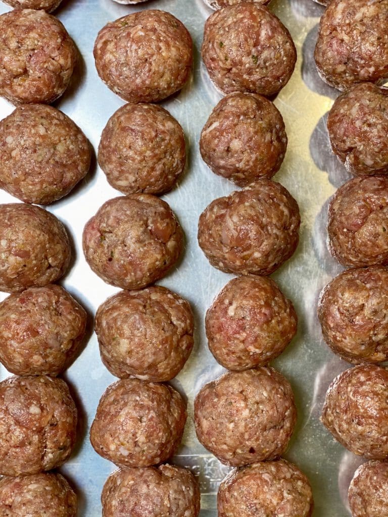 Raw meatballs on an aluminum cookie sheet.