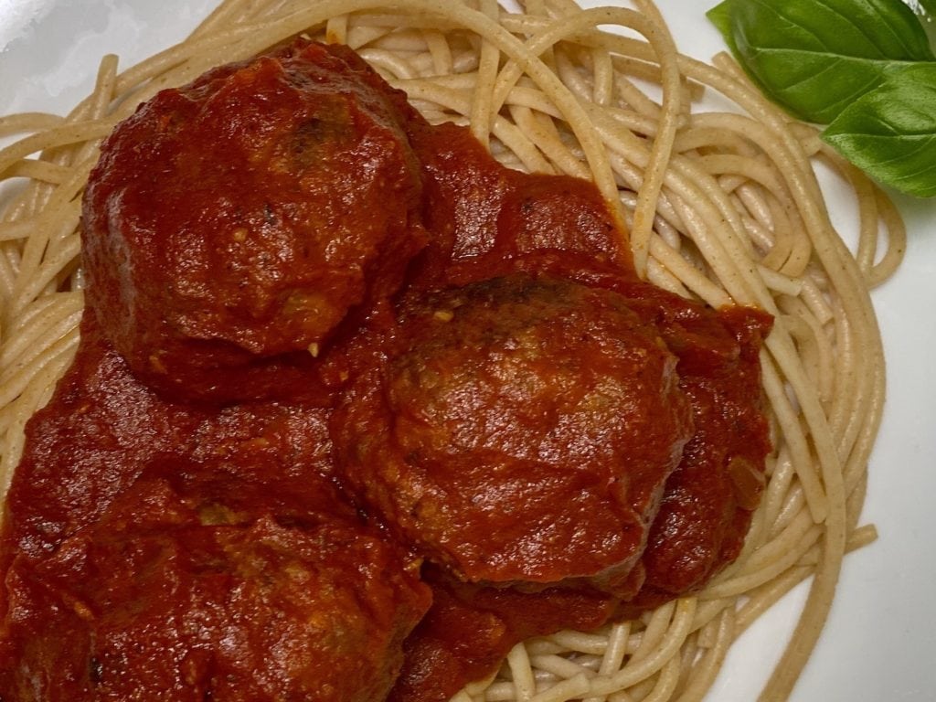 Meatballs and marinara close up on a bed of spaghetti.