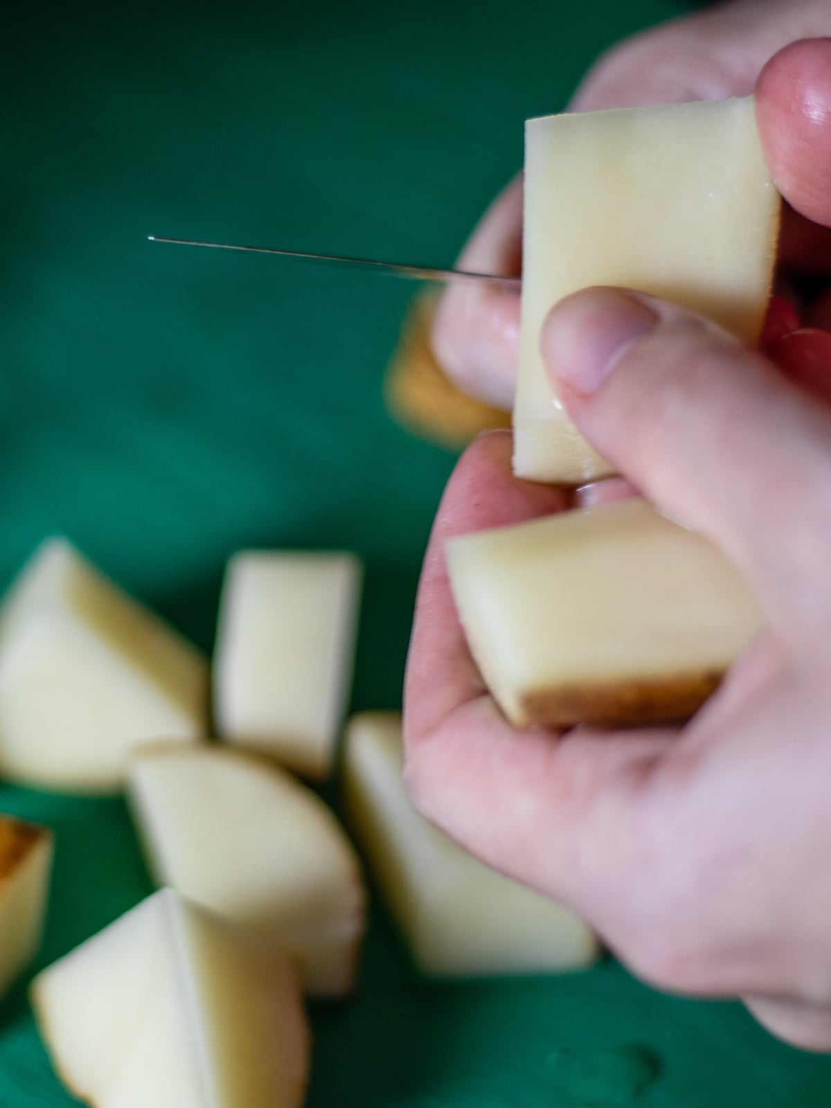 Slicing raw potatoes with a knife over a green cutting board.