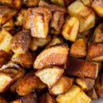 Close up of browned roasted potatoes with a light sprinkle of kosher salt on a white dish.
