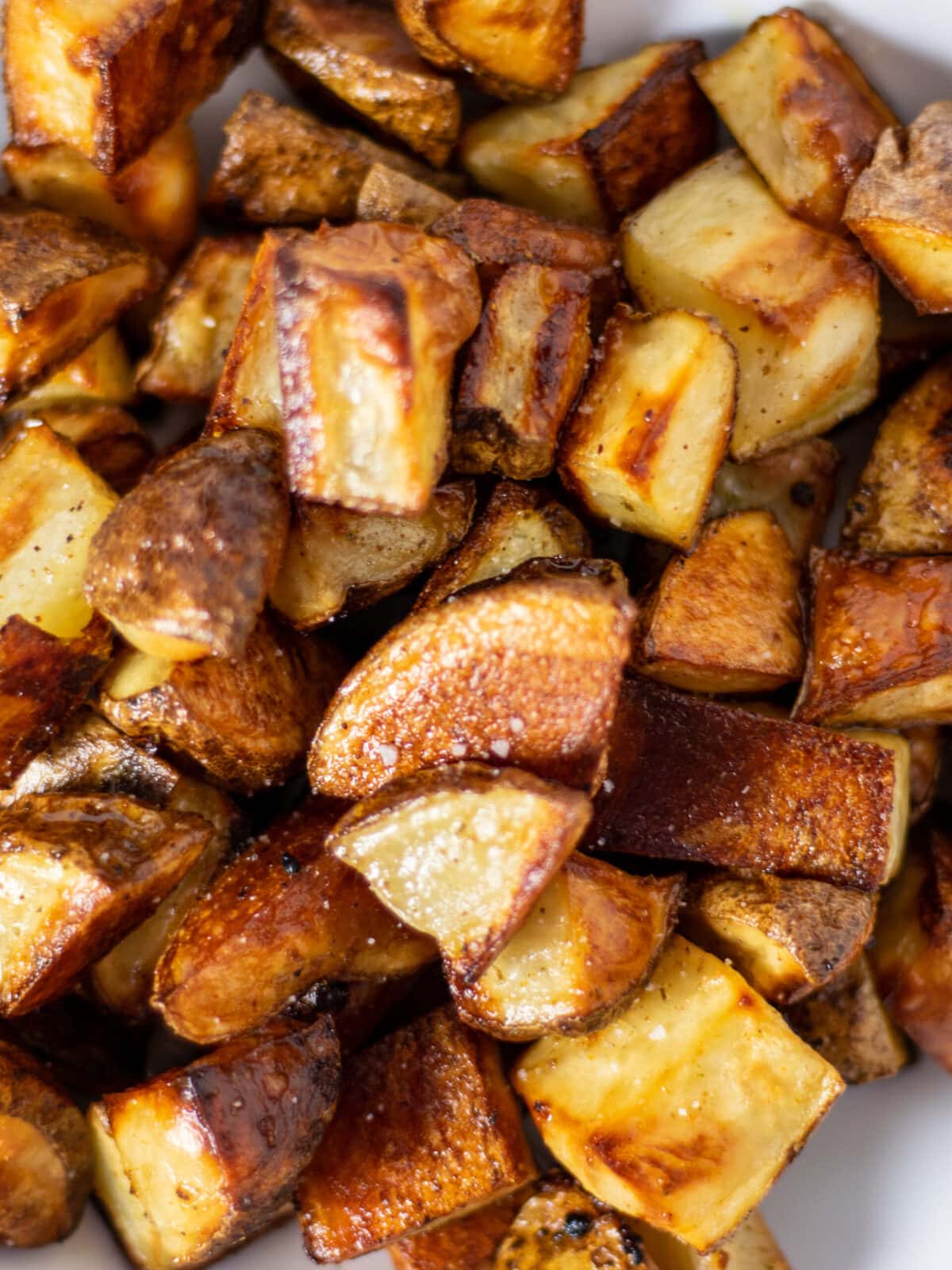 Close up of browned roasted potatoes with a light sprinkle of kosher salt on a white dish.