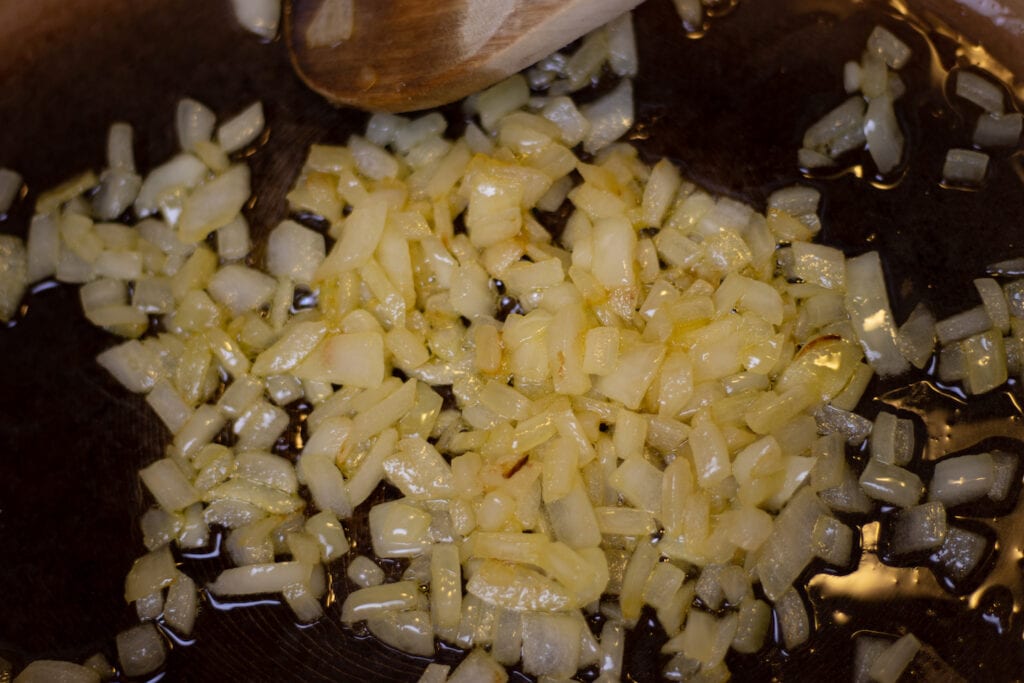 Diced onions simmering in olive oil with a wooden spoon.