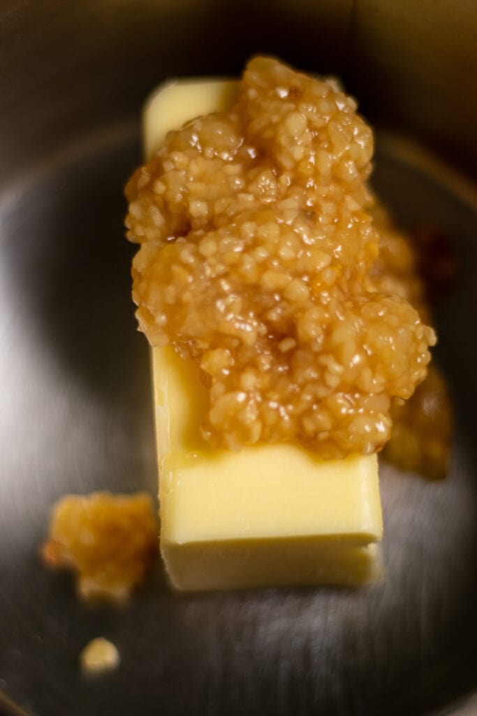 A stick of butter in an sauce pot with minced garlic piled on top of it. 