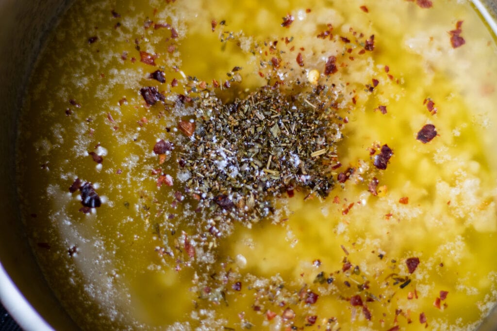 Melted butter in a sauce pan with herbs on top and garlic melting in the bottom.