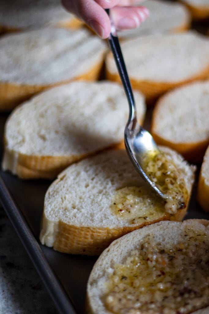 A spoon placing garlic butter on slices of french bread