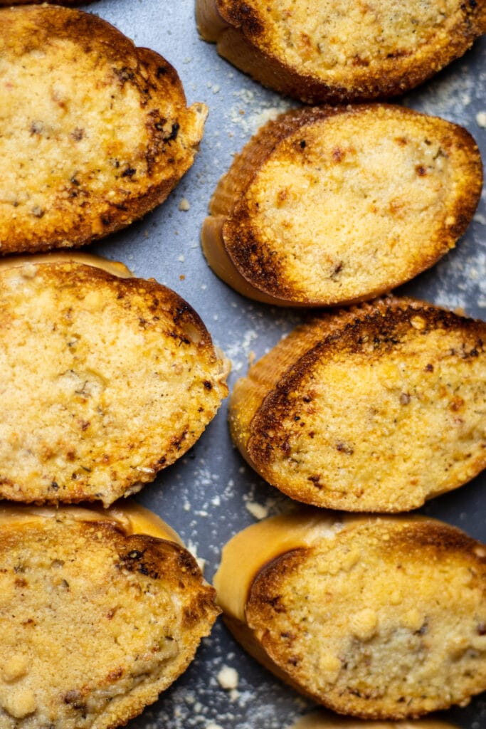 Slices of bread topped with Parmesan cheese and toasted on a cookie sheet