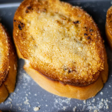 close up of some garlic bread toasted with brown portions around the crust and tanned parmesan cheese on top.