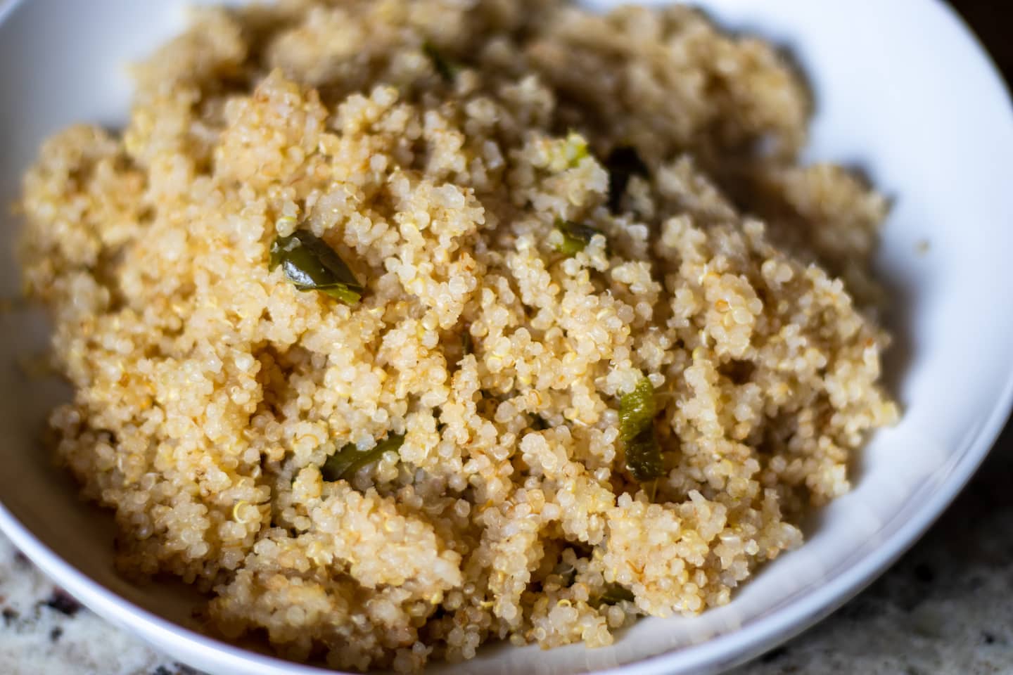 Quinoa in a white bowl with flecks of jalapeño peppers.