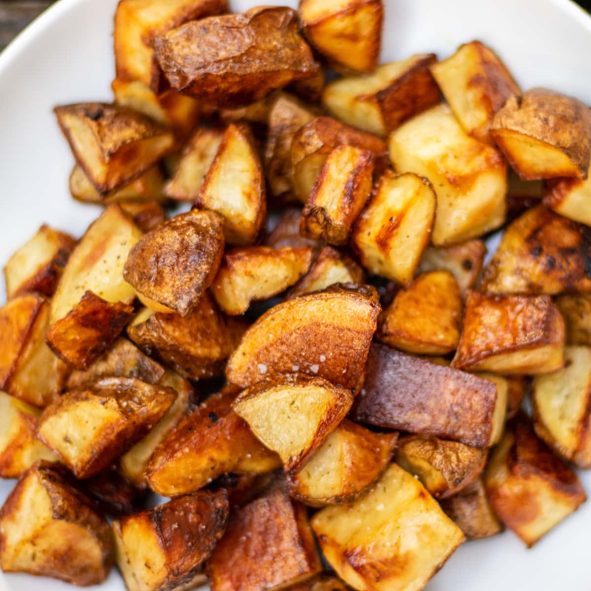 Close up of browned roasted potatoes with a light sprinkle of kosher salt on a white dish.