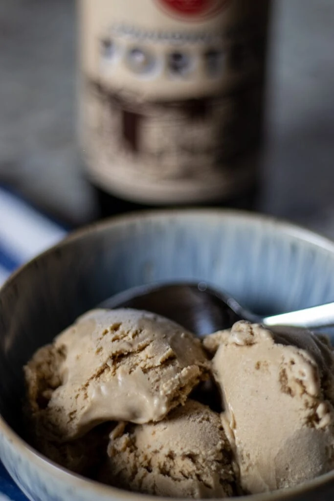 close up of tan porter ice cream in a bowl with a blurred bottle of porter in the back ground.