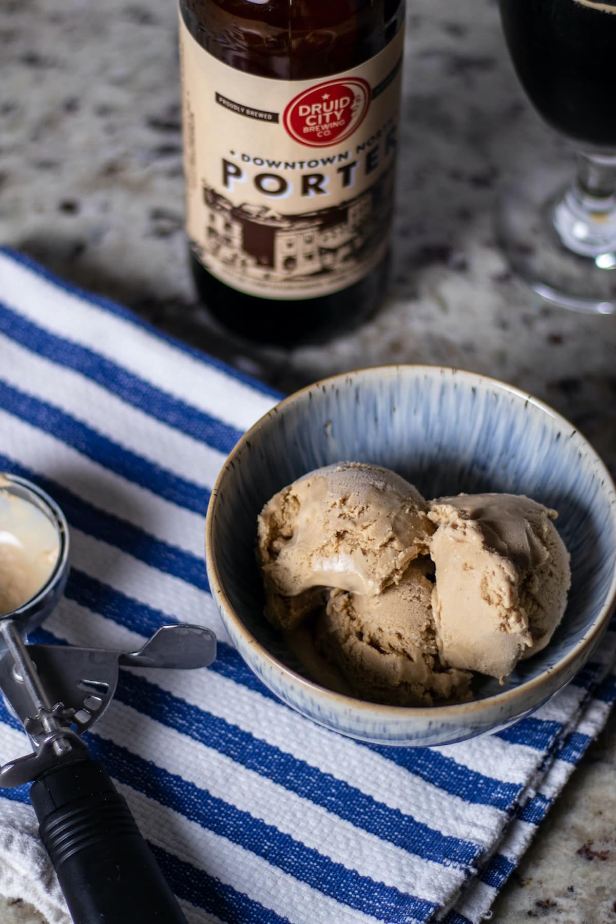 tan porter ice cream in a bowl on a striped towel with an ice cream scoop off to the left and bottle of porter just going off frame at the top center.