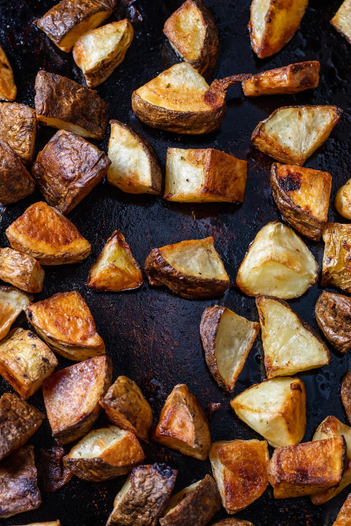 Darkly crips roasted potatoes on a lightly oiled deeply blackened cookie sheet