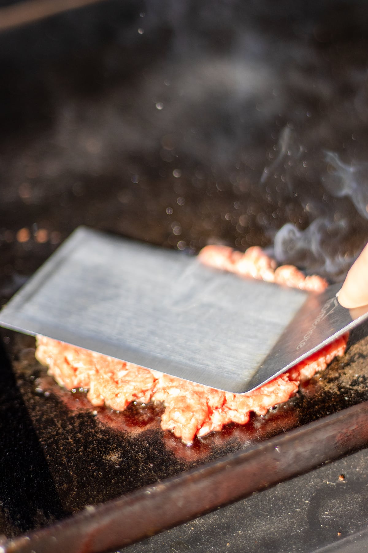 a burger patty being smashed on a griddle