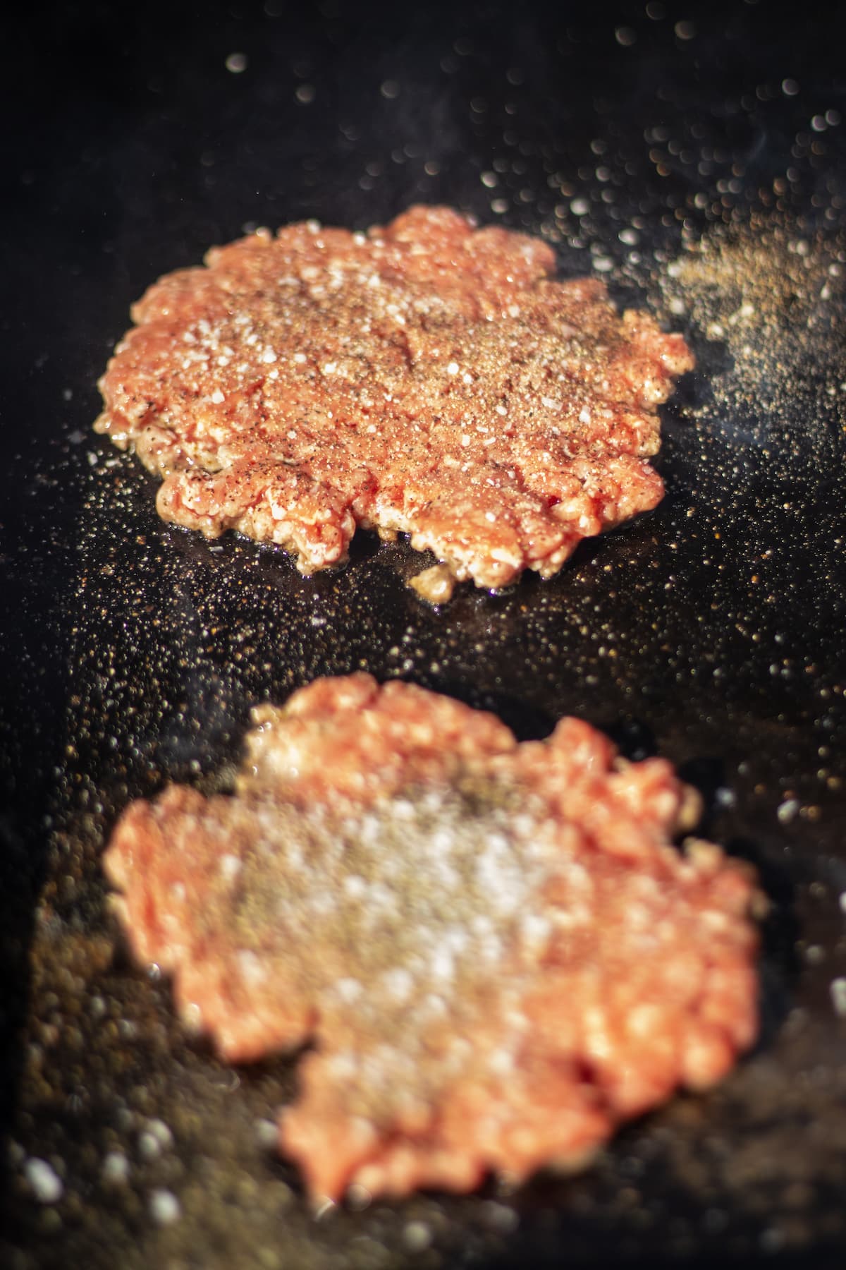 Burger patties that have been pressed on a griddle and seasoned with salt and pepper