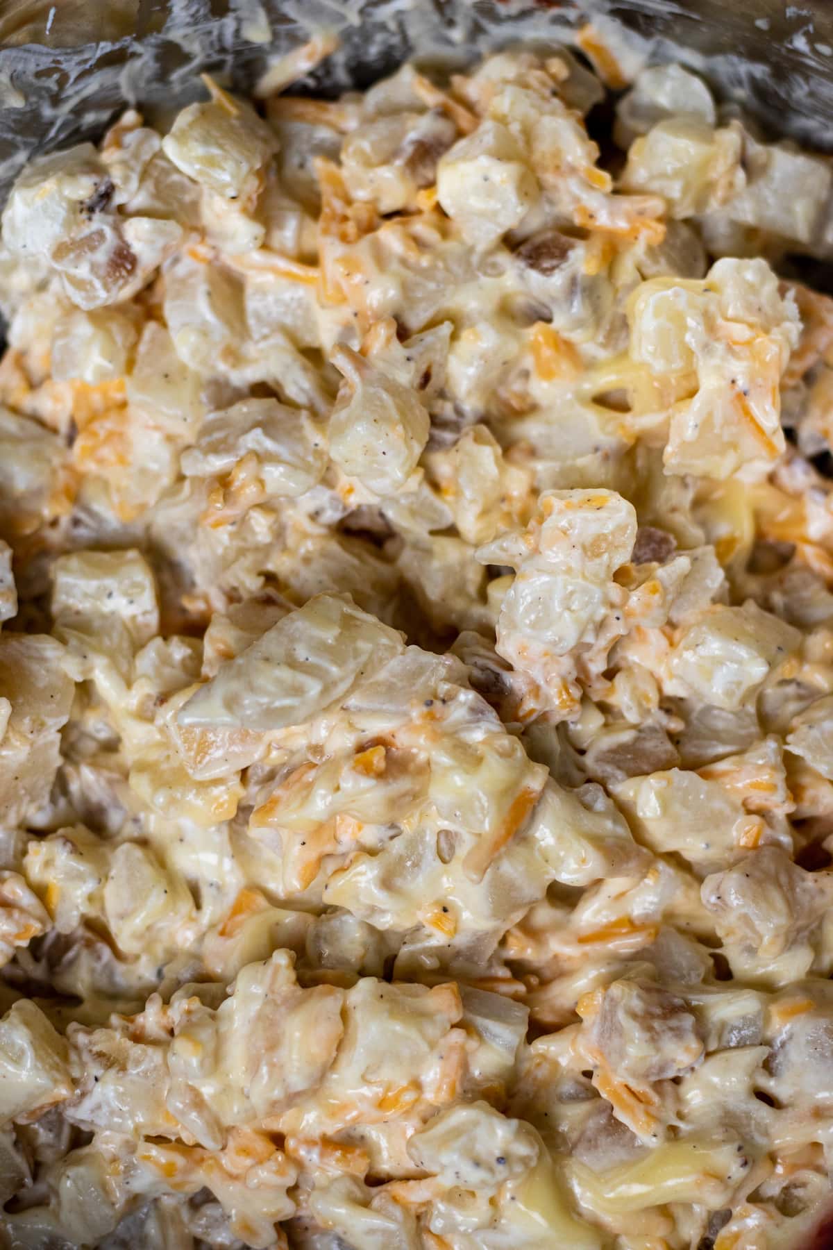 Potatoes mixed with cheddar cheese, sour cream, and cream of chicken soup in a mixing bowl.