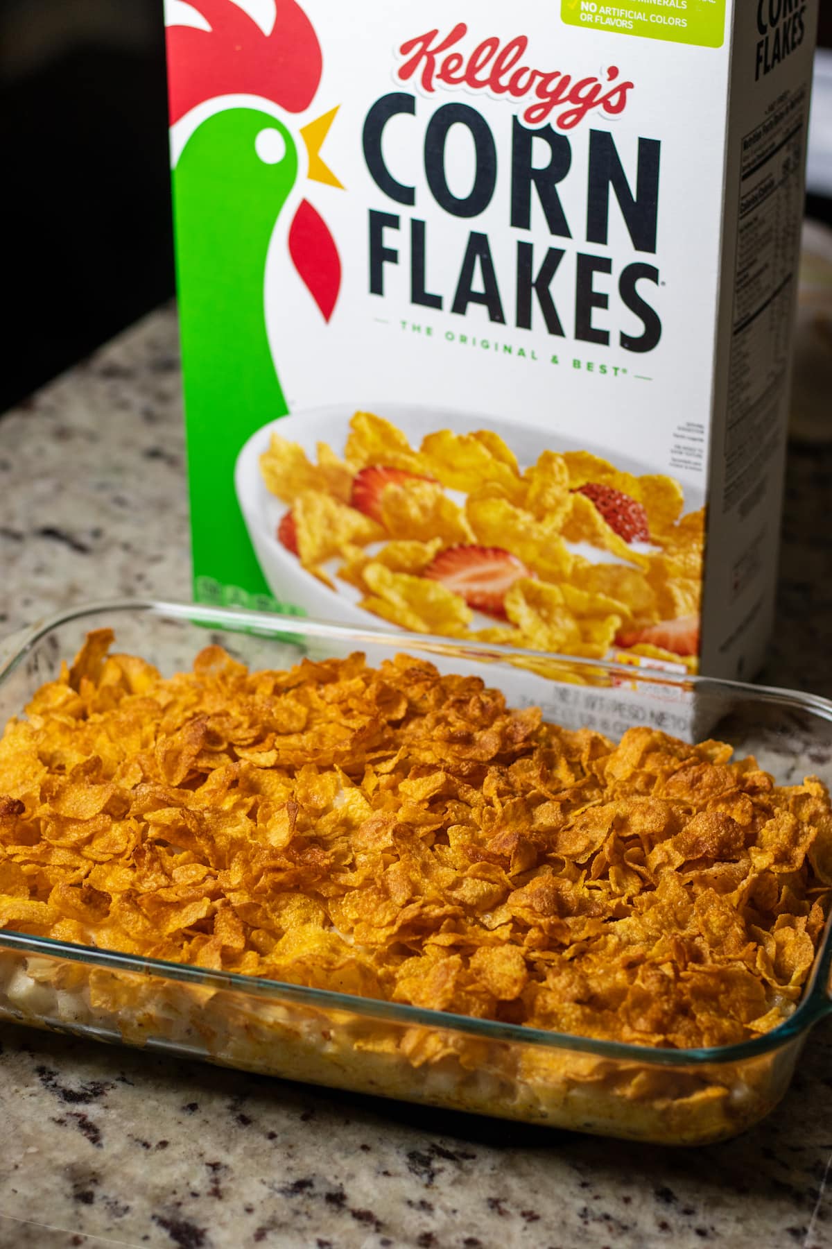 a finished casserole in front of a box of corn flakes.