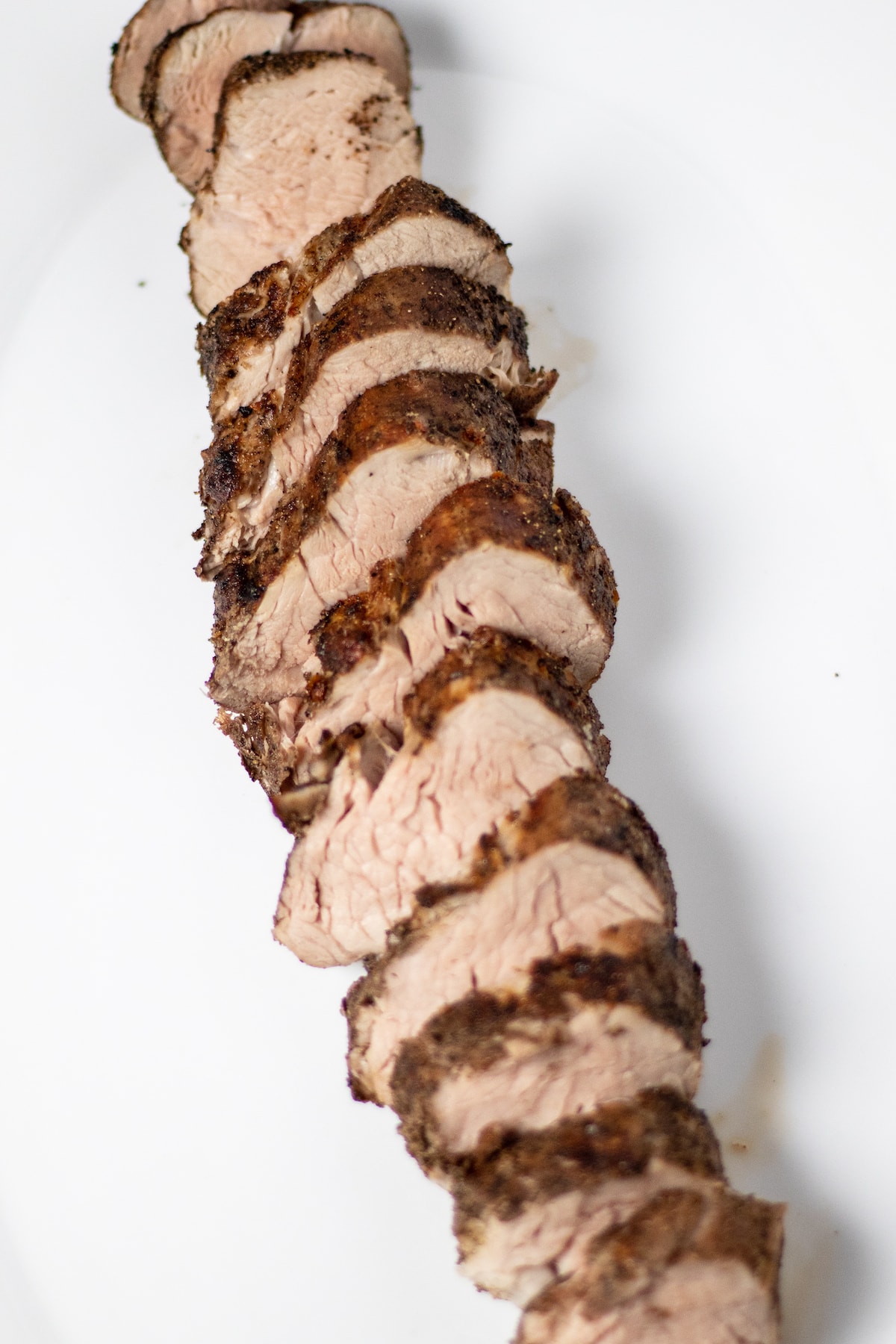 Slice pork tenderloin on a white platter shot from above.