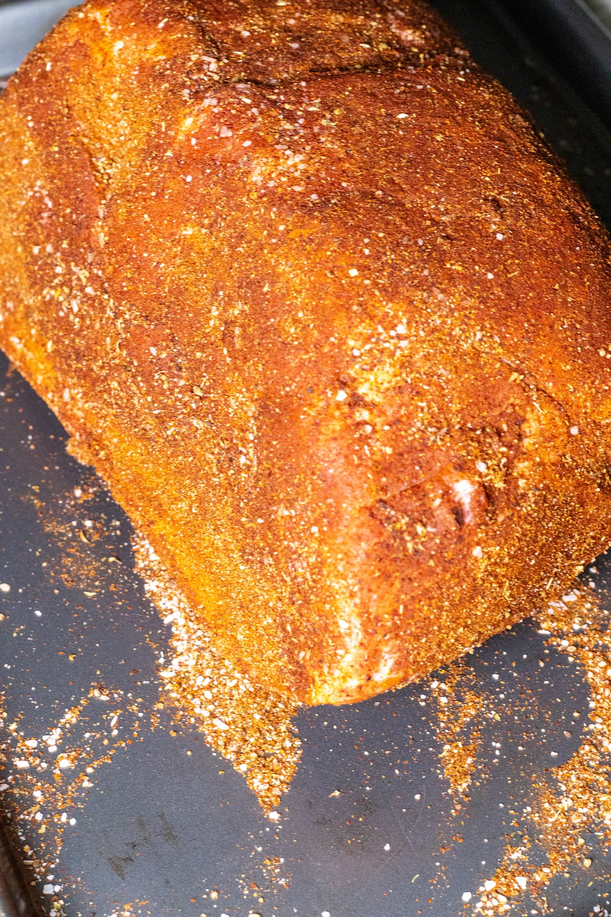 A raw pork butt covered in BBQ rub.