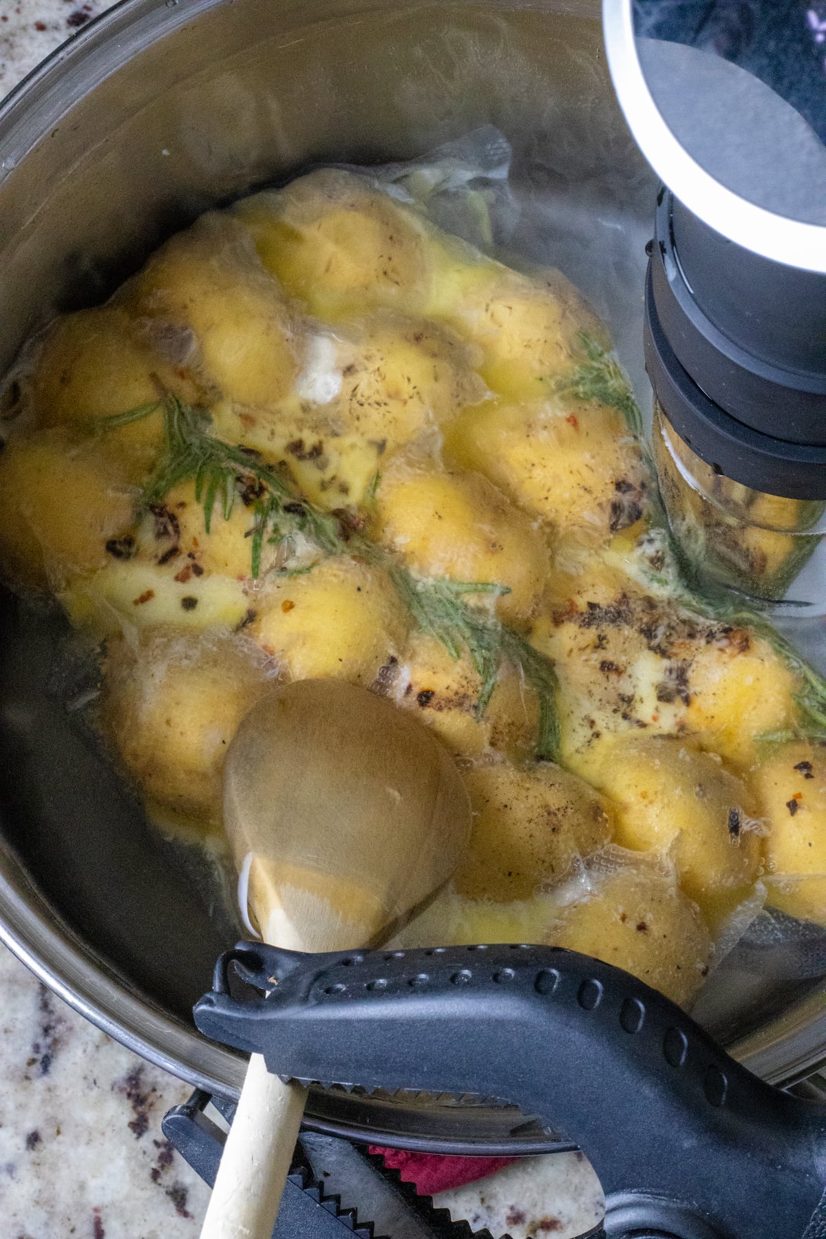 Sous vide potatoes held down by a wooden spoon. 