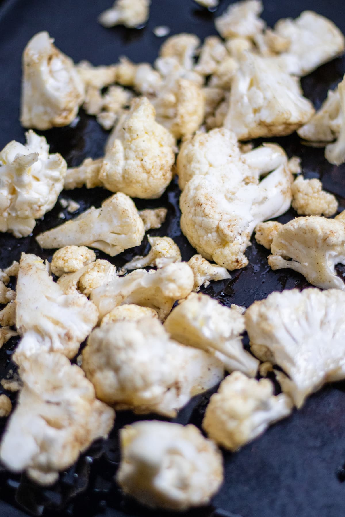 Raw and seasoned cauliflower on a baking pan.